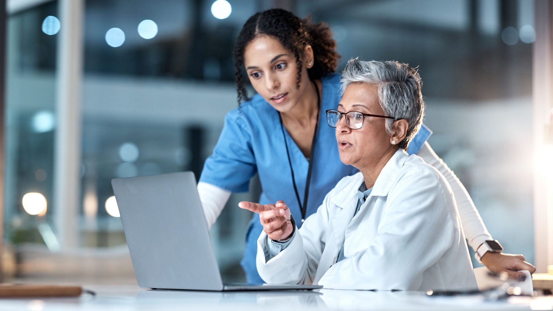 two healthcare workers discussing something on laptop